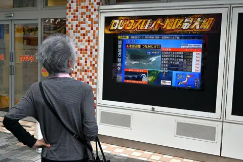 Getty Images A woman watches a television broadcast of a tsunami warning for much of coastal Japan following a 8.7 magnitude quake in the sea off eastern Russia