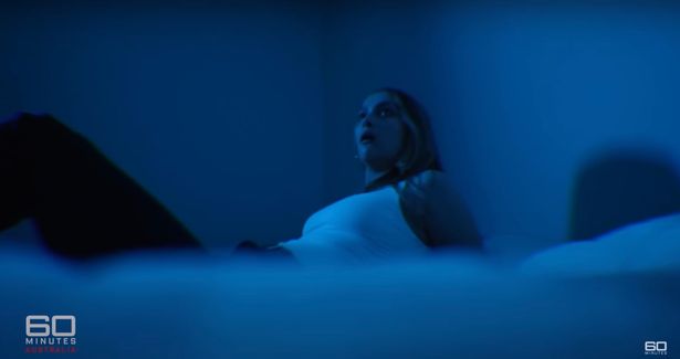A woman on a bed looking scared on a bed in a documentary re-enactment