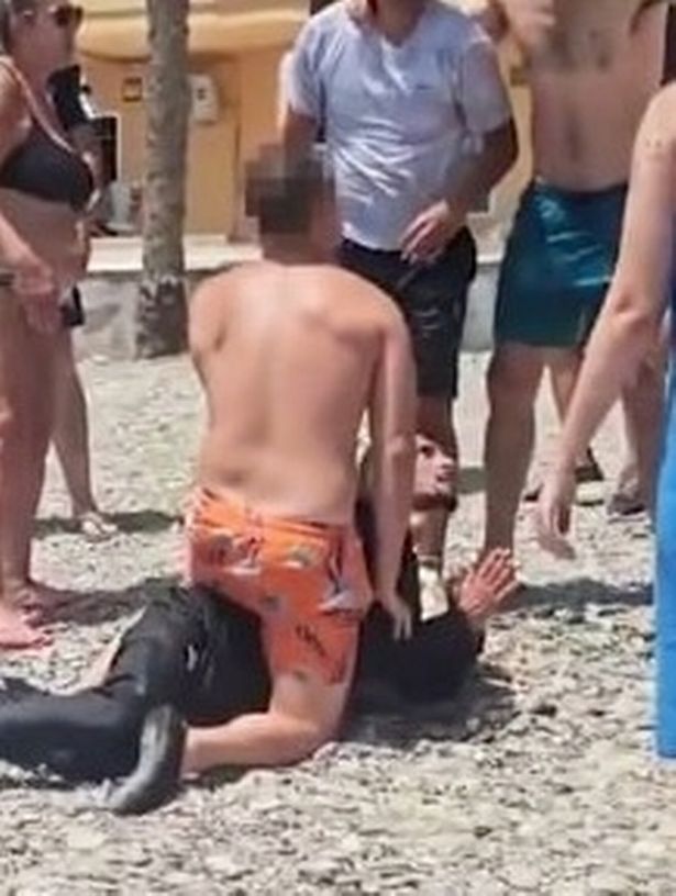A sunseeker is seen holding down one of the migrants who arrived on the busy beach moments earlier