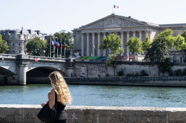 A woman walks past the Seine River and the French National Assembly, the lower House of Parliament, in Paris on August 11, 2025, amid a heatwave in Europe. (Photo by Martin LELIEVRE / AFP) (Photo by MARTIN LELIEVRE/AFP via Getty Images)