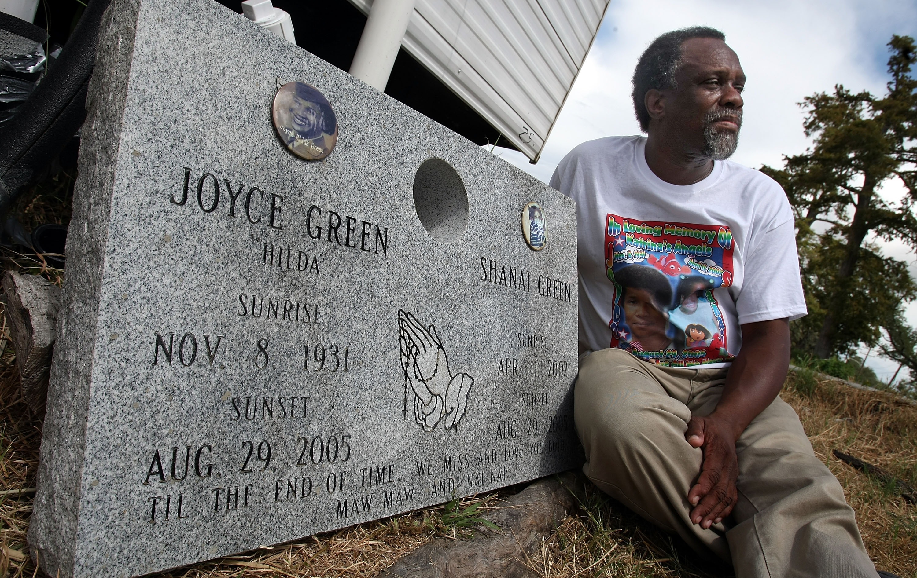 A photo of a man in a white t-shirt and brown slacks sitting next to a gray headstone. The headstone and t-shirt he's wearing acknowledge the lost lives of his mother and granddaughter.