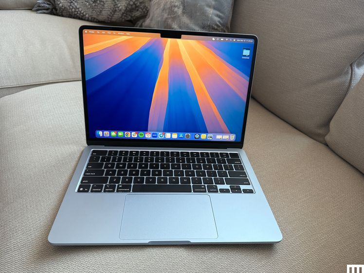 Front view of an open Apple MacBook Air 13-inch 2025 laptop sitting on a couch with the screen showing the desktop