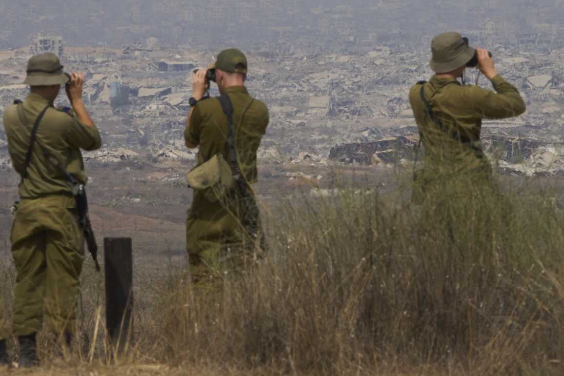 Israeli soldiers uses binoculars to look at damaged buildings in the Gaza Strip, from southern Israel, Wednesday, Aug. 13, 2025.