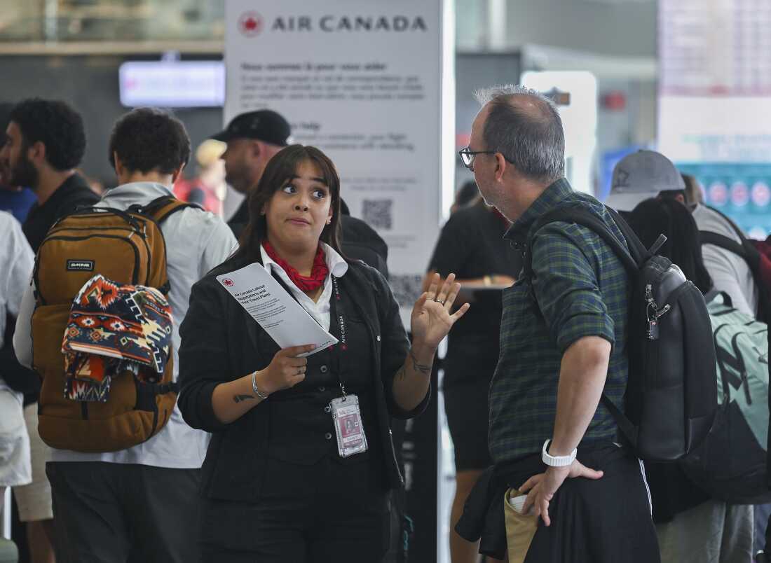 An Air Canada agent, left, talks with a man as Air Canada flight attendants strike at Montreal-Pierre Elliott Trudeau International Airport in Montreal, Saturday, Aug. 16, 2025.