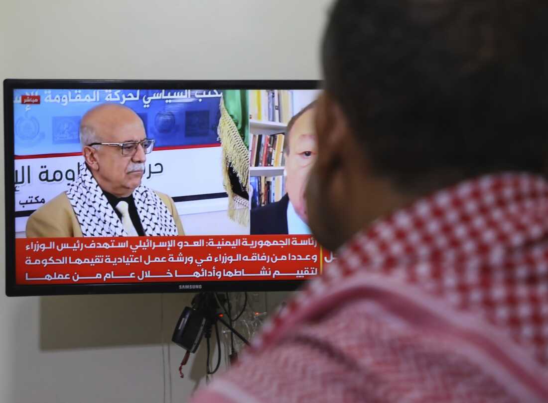 A man watches the news on TV, displaying footage of Ahmed al-Rahawi, the prime minister of the Houthi-controlled government, who was killed, along with others, in Thursday