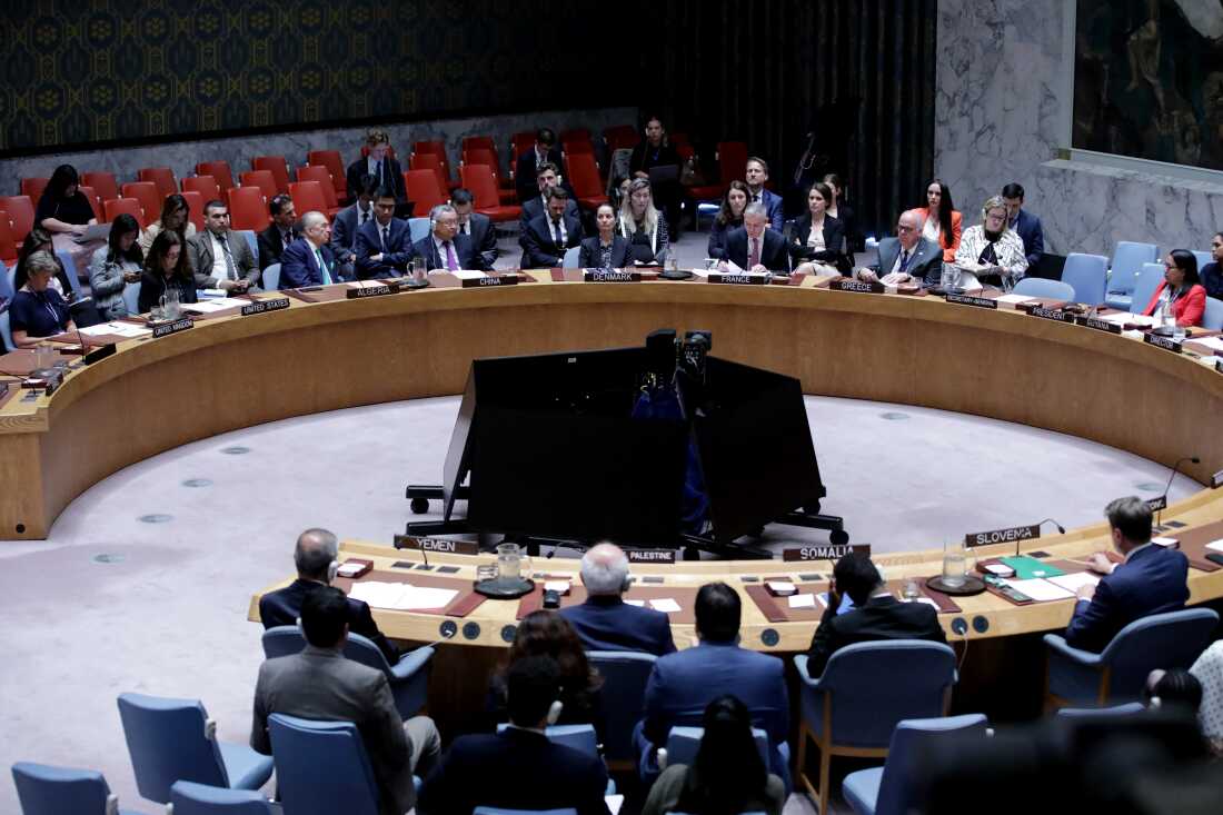 Members of the United Nations Security Council sit around a large horseshoe-shaped desk as they vote on a resolution.