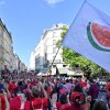 A white flag with a large watermelon slice on it is waved during the Red Line for Gaza protest in Paris on July 8. Most of the protesters are wearing red shirts, and they're walking down a street lined by multistory buildings.