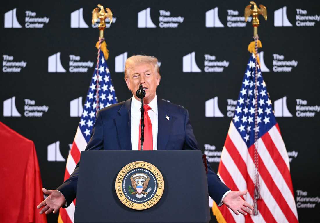 President Trump speaks from behind a lectern with the presidential seal on the front of it. Behind him are two American flags and a backdrop that says:
