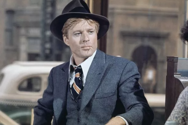 American actor Robert Redford wearing a grey tweed blazer over a matching waistcoat and a white shirt, with a diagonally striped tie, with a grey fedora, in a scene from