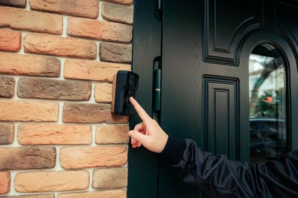 man hand in a black jacket rings the door intercom. orange brick wall (
