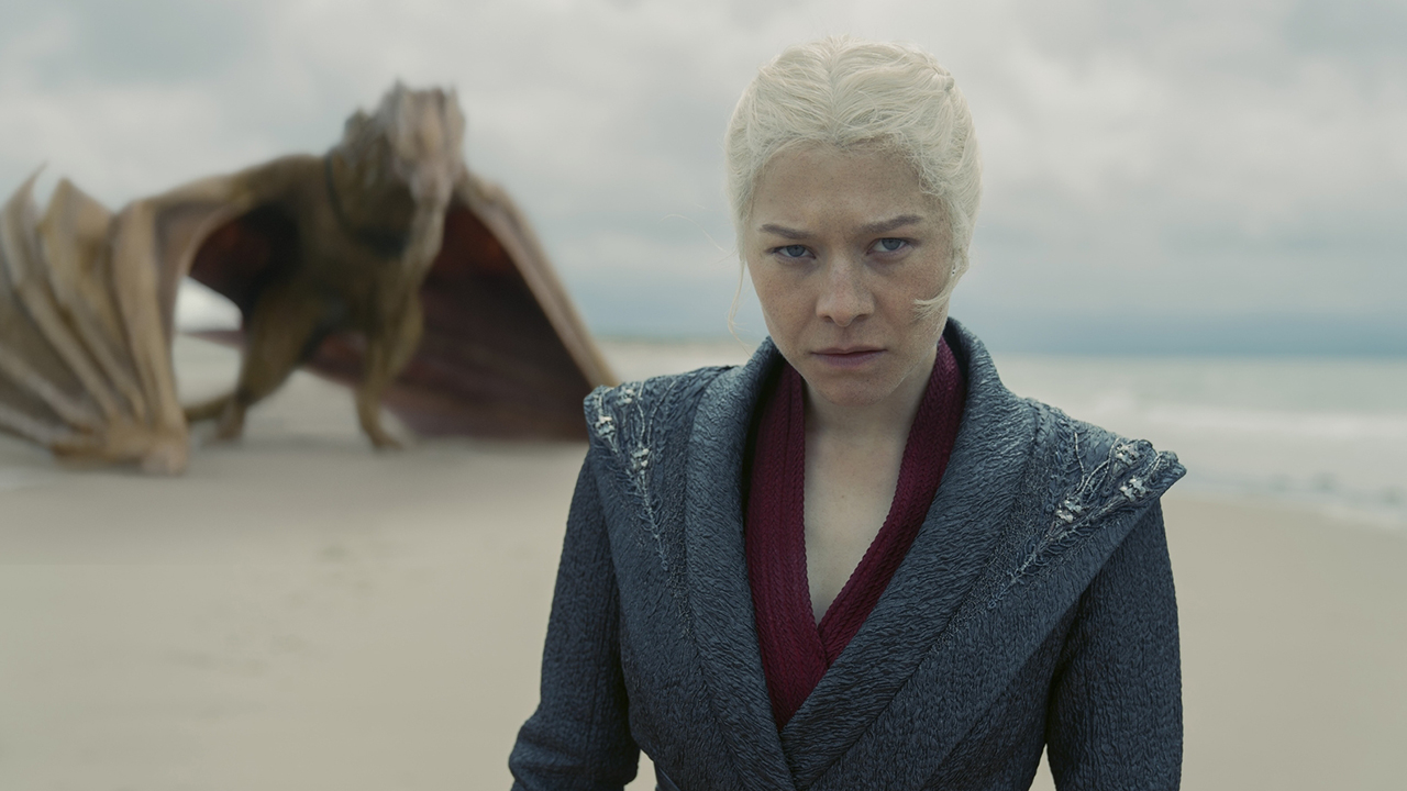 Rhaenyra Targaryen scowling as she stands on a beach with Syrax in the background in House of the Dragon season 2