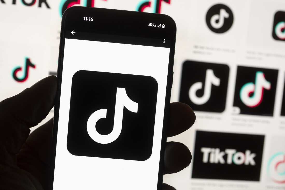 The TikTok logo is seen on a mobile phone in front of a computer screen which displays the TikTok home screen, Oct. 14, 2022, in Boston.