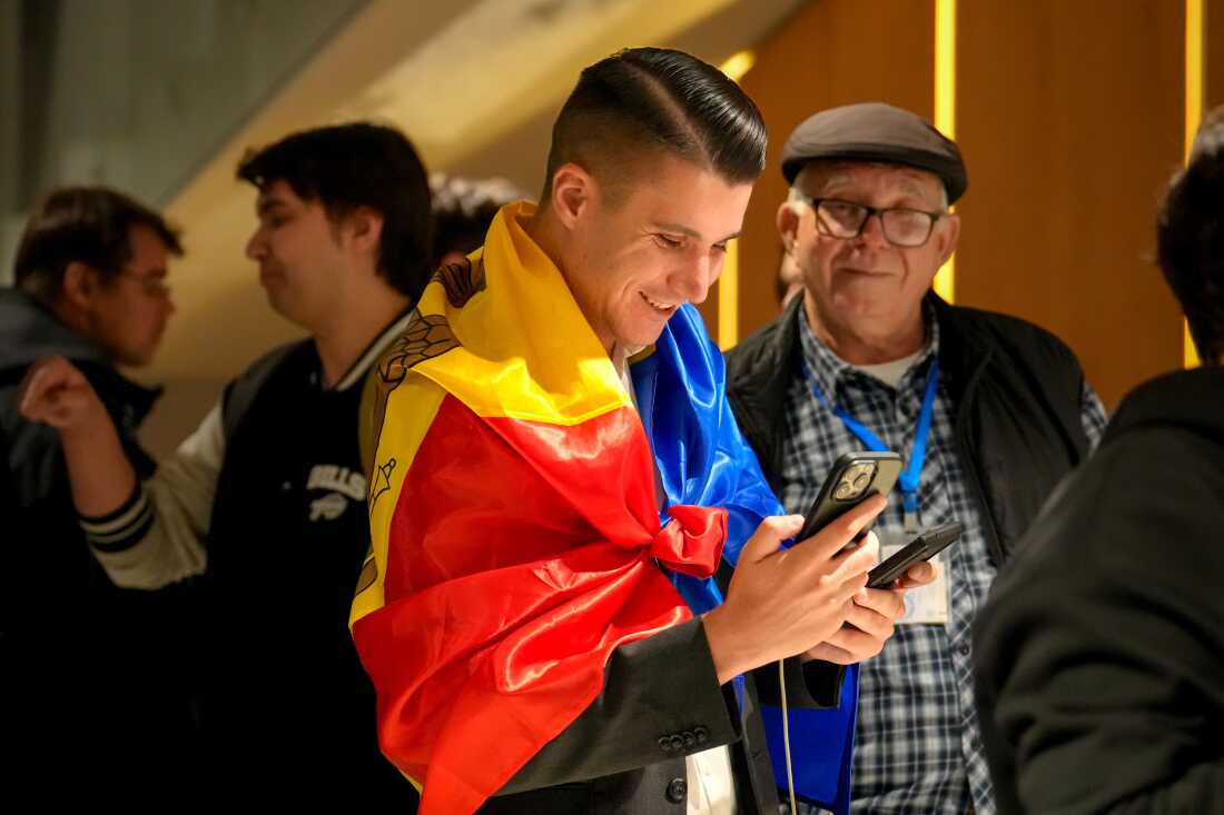 A supporter of the pro-EU Party of Action and Solidarity (PAS) draped in the Moldovan flag smiles as he checks partial results on a phone after the polls closed for the parliamentary election, in Chisinau, Moldova, Sunday, Sept. 28, 2025.