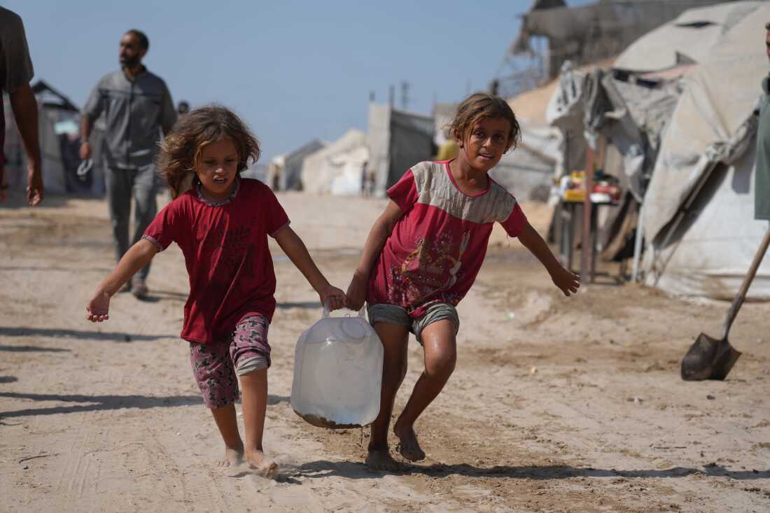 Displaced Palestinians girls carry a jerrycan after collecting water from a distribution point at a tent camp in Muwasi, an area that Israel has designated as a safe zone, in Khan Younis southern Gaza Strip, Monday, Sept. 29, 2025. (AP Photo/Jehad Alshrafi)