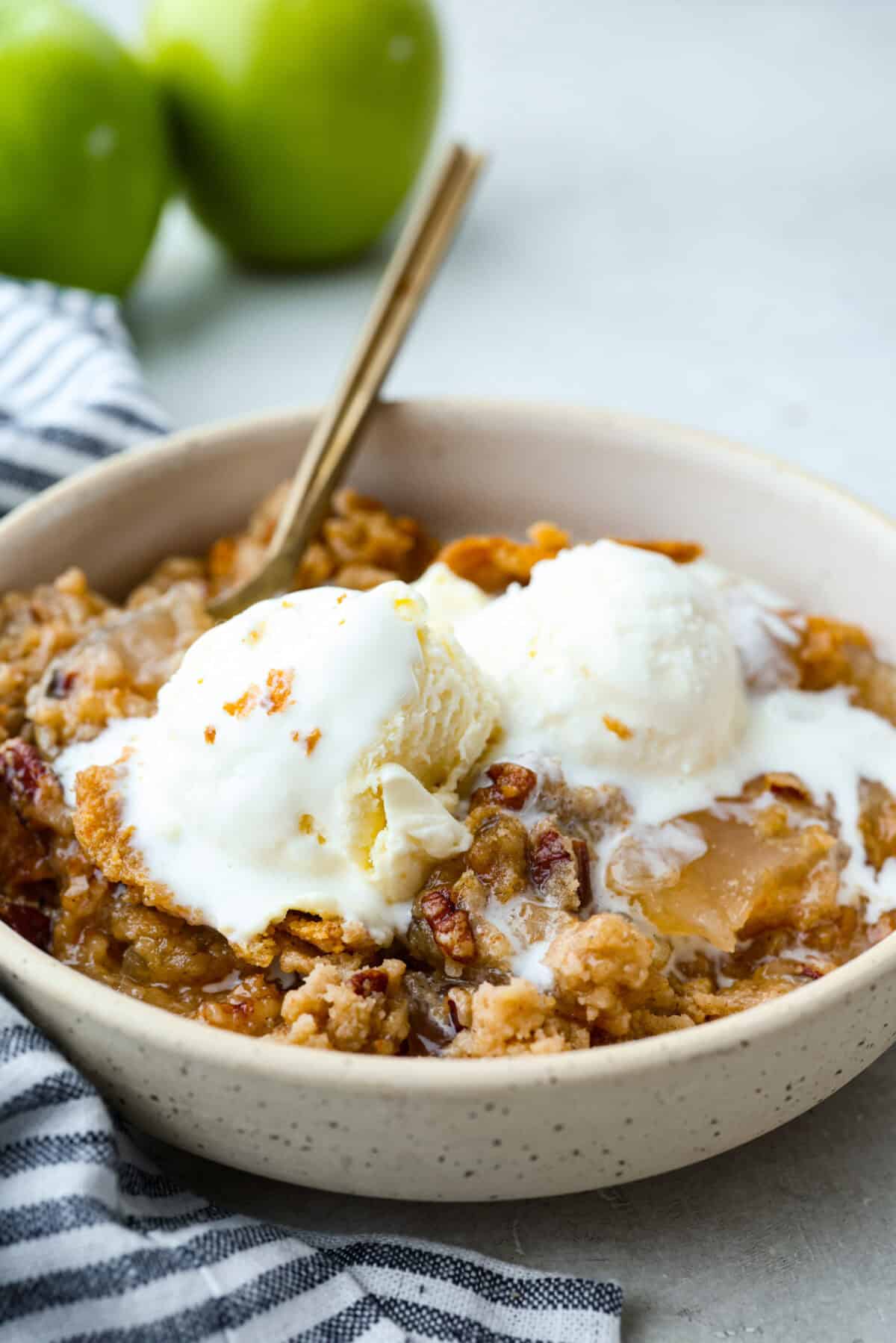 Bowl of apple dump cake with vanilla ice cream on top.