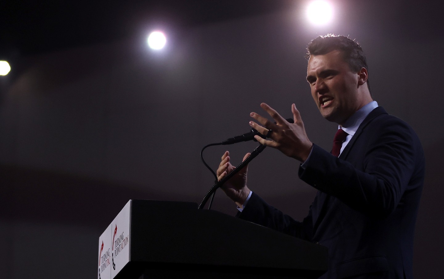 Charlie Kirk at a podium against a dark background.