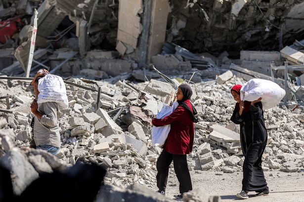 People walk past rubble, carrying sacks of flour, outside destroyed buildings in the centre of Khan Yunis