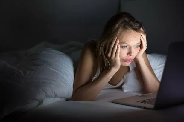Pretty young woman watching something awful/sad on her laptop in bed at night in a dark bedroom (shallow DOF; color toned image)