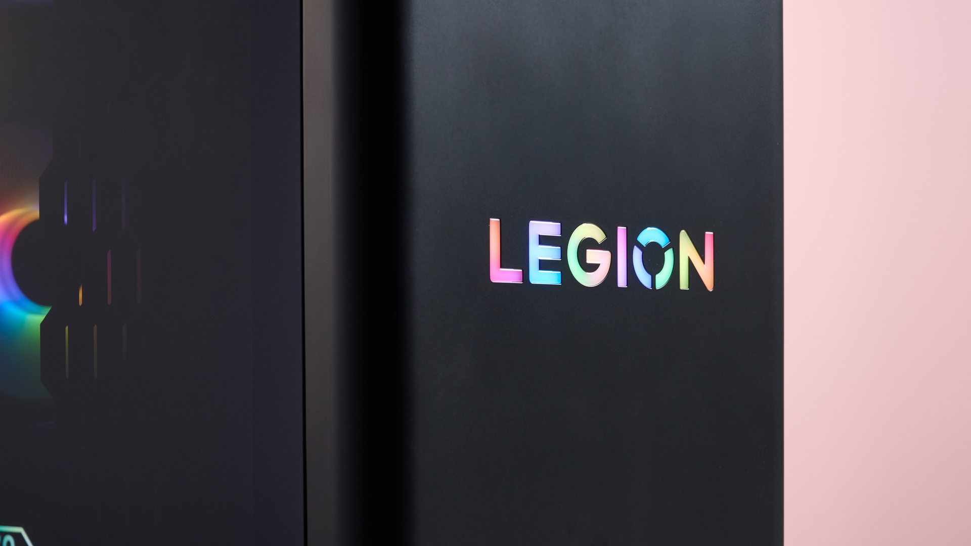 Close-up of "LEGION" logo on front of the Lenovo Legion Tower 5 RGB lighting on, with pink wall in background