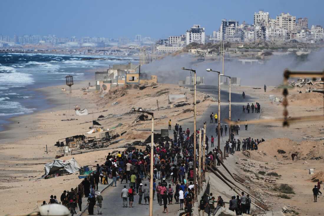 Displaced Palestinians gather on the coastal road near Wadi Gaza after the announcement that Israel and Hamas had agreed to the first phase of a peace plan to pause the fighting, as Israeli tanks block the road leading to Gaza City, in the central Gaza Strip, Thursday, Oct. 9, 2025. (AP Photo/Abdel Kareem Hana)