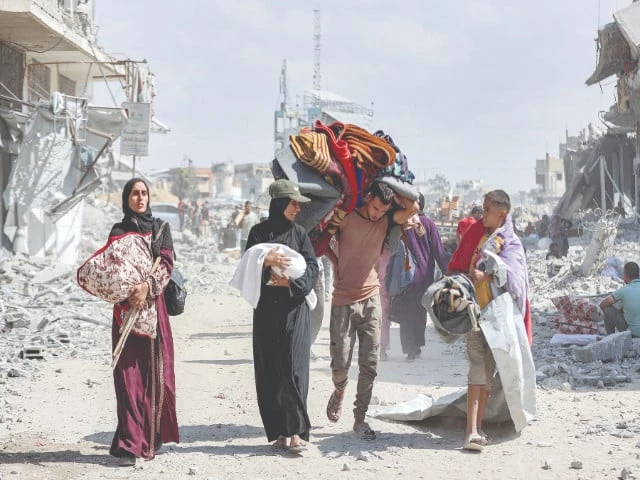 a woman carrying a child speaks with another boy as they walk with other people past the rubble of destroyed buildings in the centre of khan yunis in the southern gaza strip photo afp