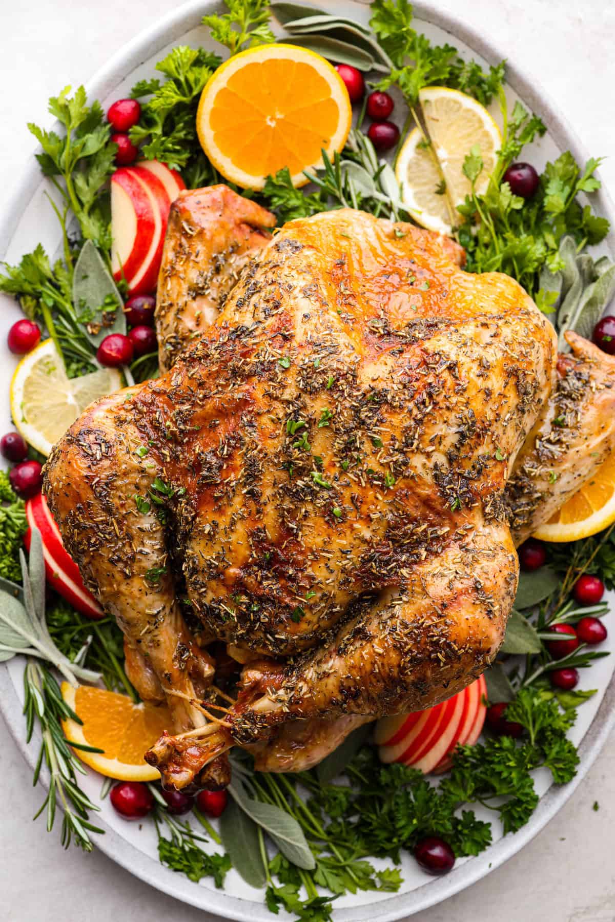 A cooked golden turkey plated with herbs and fruits.